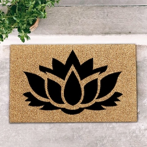 Puede incluir: Una alfombra de coco marrón con un diseño de flor de loto negro.