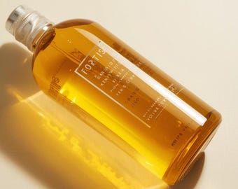 May include: A clear glass bottle filled with a golden liquid, featuring a silver cap. The label displays the word "FORTISE" and other text. The bottle is angled, with light reflecting off its surface.