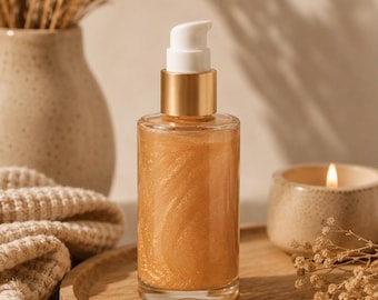 May include: A clear glass bottle filled with a shimmering gold liquid, featuring a gold-colored collar and a white pump dispenser top. The cylindrical bottle contains a viscous, metallic-toned substance with visible swirling patterns inside.