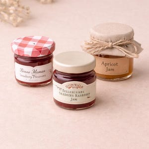 May include: Three small jars of preserves. One jar has a red and white checkered lid and a label that reads "Bonne Maman Strawberry Preserves." Another jar has a white lid and a label that reads "Stonewall Kitchen Seeders Rasberry Jam." The third jar has a tan lid and a label that reads "Apricot Jam."