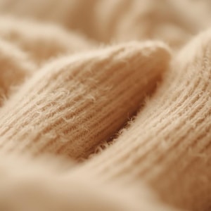 May include: Close-up of two beige knitted socks. The socks have a ribbed texture and a soft, fuzzy appearance. The image is well-lit, highlighting the details of the knitwear. The socks appear to be made of a warm, comfortable material.