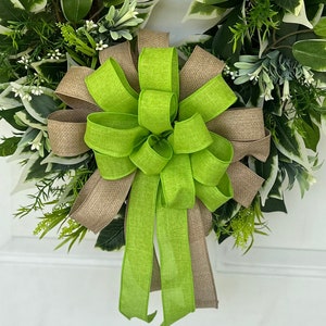 May include: A green and brown bow with a burlap texture. The bow is tied to a wreath of green leaves.