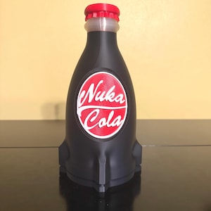 May include: A black Nuka Cola bottle with a red cap and a white and red logo. The bottle has a unique rocket-like shape and is likely a collectible item or a decorative piece.