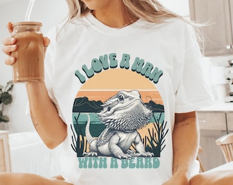 May include: White t-shirt with a retro sunset graphic and a bearded dragon. The text "I love a man with a beard" is printed on the shirt.