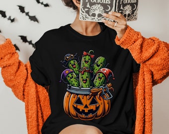 May include: A black t-shirt with a graphic of a jack-o'-lantern filled with green pickles wearing Halloween costumes.