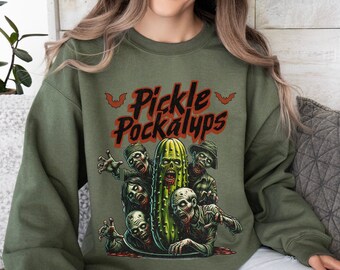 May include: A green sweatshirt with a graphic of a pickle surrounded by zombie-like figures. The text "Pickle Pockalypse" is printed in orange above the graphic.