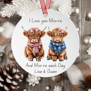 May include: A white round ornament with a picture of two brown Highland cows wearing scarves and bows. The text "I Love you Moo-re And Moo-re each Day Lisa & Owen" is printed on the ornament.