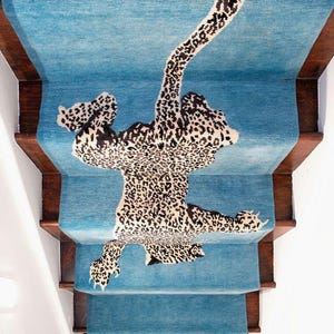 May include: A blue stair runner featuring a leopard print design. The leopard pattern is in black, brown, and cream. The stairs have wooden trim. The runner covers the steps and risers.