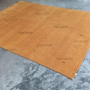 May include: A large, rectangular, light brown rug with a subtle woven texture. The rug is laid out on a concrete floor.
