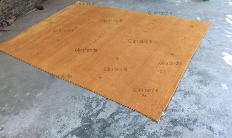 May include: A large, rectangular, light brown rug with a subtle woven texture. The rug is laid out on a concrete floor.