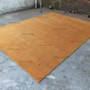 May include: A large, rectangular, light brown rug with a subtle texture. The rug is lying flat on a concrete floor.