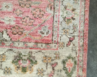 May include: Close-up of a pink and cream-colored rug with a floral pattern. The rug has a textured surface and a fringe along the bottom edge. The design includes shades of pink, green, and cream.