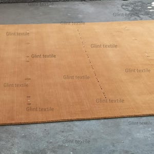 May include: A large, rectangular, light brown rug with a subtle texture. The rug is made of natural fibers and has a simple, elegant design.