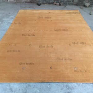 May include: A large, rectangular, light brown rug with a subtle texture. The rug has a simple design with a few small, dark markings.