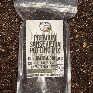 May include: A clear plastic bag filled with a dark brown potting mix for Sansevieria plants. The bag has a white label with the text "Rooting for you Plant Nursery" and "Premium Sansevieria Potting Mix". The label also states that the mix is 100% natural and organic, soil free, peat free, and perlite free. It is handcrafted in small batches.