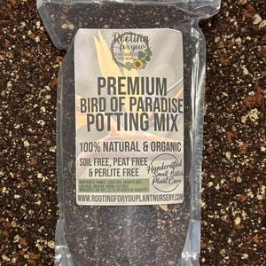 May include: A clear plastic bag filled with a dark brown potting mix. The bag has a white label with the text "Rooting for you Plant Nursery" and "Premium Bird of Paradise Potting Mix". The label also states "100% Natural & Organic", "Soil Free, Peat Free & Perlite Free", and "Handcrafted Small Batch Plant Care".