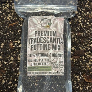 May include: A clear plastic bag filled with a dark brown potting mix for Tradescantia plants. The bag has a white label with the text "Rooting for you Plant Nursery" and "Premium Tradescantia Potting Mix". The label also states that the mix is 100% natural and organic, soil free, peat free, and perlite free. The ingredients are listed as pumice, coco coir, bark nuggets, and worm castings. The label also includes the website address "www.rootingforyouplantnursery.com".