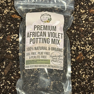 May include: A clear plastic bag filled with a dark brown potting mix for African violets. The bag has a white label that reads "Premium African Violet Potting Mix 100% Natural & Organic Soil Free, Peat Free & Perlite Free Handcrafted Small Batch Plant Care www.rootingforyouplantnursery.com"