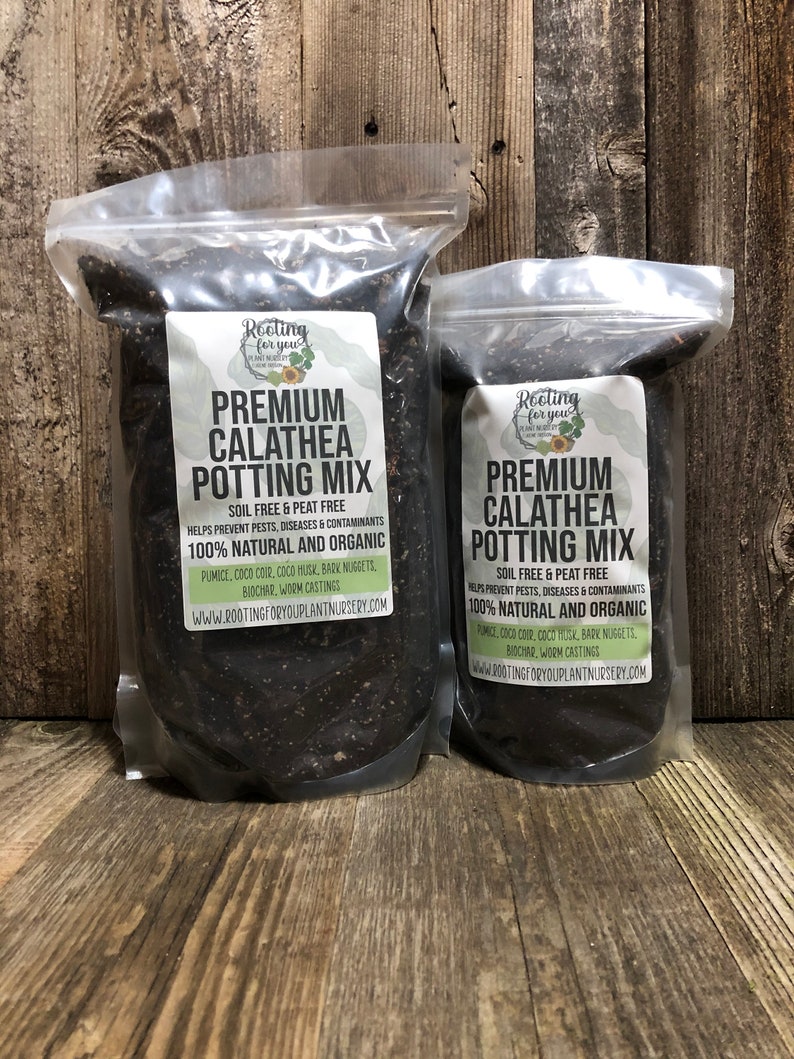 May include: Two bags of potting mix labeled "Premium Calathea Potting Mix" with the text "Soil Free & Peat Free" and "100% Natural and Organic". The bags are on a wooden surface.