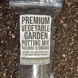 May include: A clear plastic bag filled with dark brown potting mix. The bag has a white label that reads "PREMIUM VEGETABLE GARDEN POTTING MIX NATURAL & ORGANIC SOIL FREE, PEAT FREE & PERLITE FREE PET AND HUMAN FRIENDLY INGREDIENTS INGREDIENTS ARE NOT LISTED IN ORDER OF QUANTITY ROOTING FOR YOU PLANT NURSERY - EUGENE, OREGON WWW.ROOTINGFORYOUPLANTNURSERY.COM".