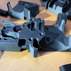 Op de afbeelding: Close-up van een zwart 3D-geprint kunststof onderdeel met ingewikkelde details en meerdere gaten. Het onderdeel lijkt een component te zijn voor een machine of apparaat.
