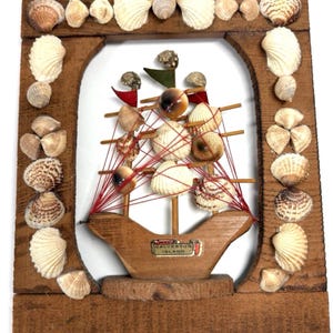 May include: A wooden key holder featuring a ship made of seashells and red string, with a "Galveston Island" label. The frame is decorated with various seashells and has three hooks at the bottom. A rope loop is at the top.