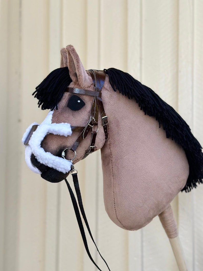Peut inclure: Une t&ecirc;te de cheval en peluche marron et noire avec une crini&egrave;re noire et une bride en cuir marron. Le cheval a un museau blanc et un nez noir. Le cheval est attach&eacute; &agrave; une r&ecirc;ne en cuir noir.