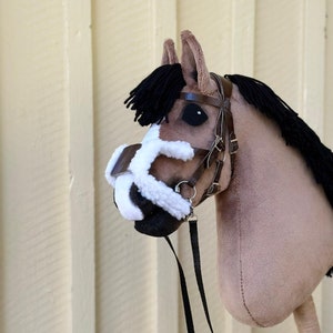 Peut inclure: Une t&ecirc;te de cheval en peluche marron et blanche avec une crini&egrave;re et une queue noires. Le cheval porte une bride en cuir marron avec un nez en polaire noir et une longe noire.