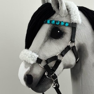 Puede incluir: Una cabeza de caballo gris con una crin negra y un bozal de cuero negro con una banda de frente de diamantes de imitaci&oacute;n turquesa. El bozal tiene una banda de nariz y una correa de garganta.