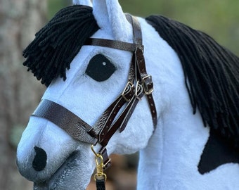 May include: A white stuffed horse with a black mane and tail, wearing a brown leather bridle with a black lead rope.