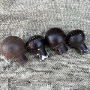 Może przedstawiać: Cztery antyczne brązowe gałki do drzwi z zaokrągloną g&oacute;rą i cylindryczną podstawą. Gałki mają wygląd vintage, niekt&oacute;re wykazują ślady zużycia i utraty farby. Ułożone są w rzędzie na teksturowanym, neutralnym tle.