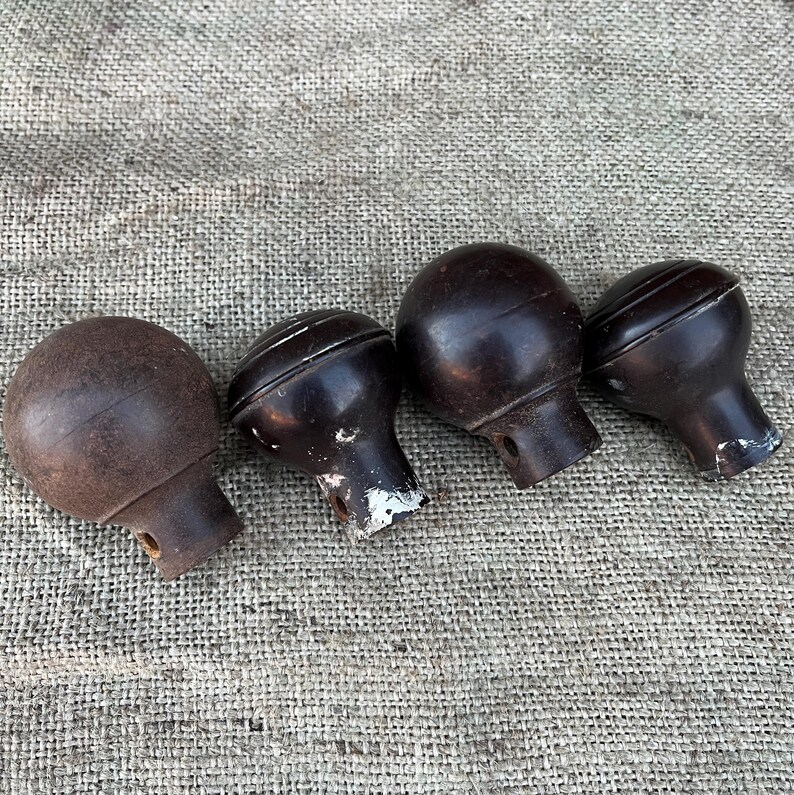 Może przedstawiać: Cztery antyczne brązowe gałki do drzwi z zaokrągloną g&oacute;rą i cylindryczną podstawą. Gałki mają wygląd vintage, niekt&oacute;re wykazują ślady zużycia i utraty farby. Ułożone są w rzędzie na teksturowanym, neutralnym tle.