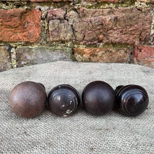 Może przedstawiać: Cztery antyczne drewniane gałki do drzwi w r&oacute;żnych odcieniach brązu. Gałki są okrągłe z gładkimi lub rowkowanymi wzorami. Ułożone są na teksturowanej, neutralnej powierzchni, z ceglaną ścianą w tle.