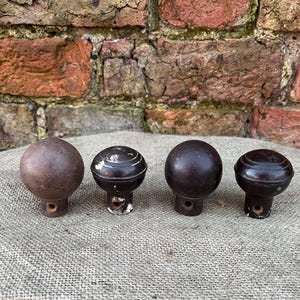 Może przedstawiać: Cztery antyczne, brązowe, drewniane gałki o okrągłym kształcie i małym otworze u podstawy. Gałki mają wygląd postarzałego, z widocznymi śladami zużycia i ubytkami farby. Ułożone w rzędzie na teksturowanej powierzchni.