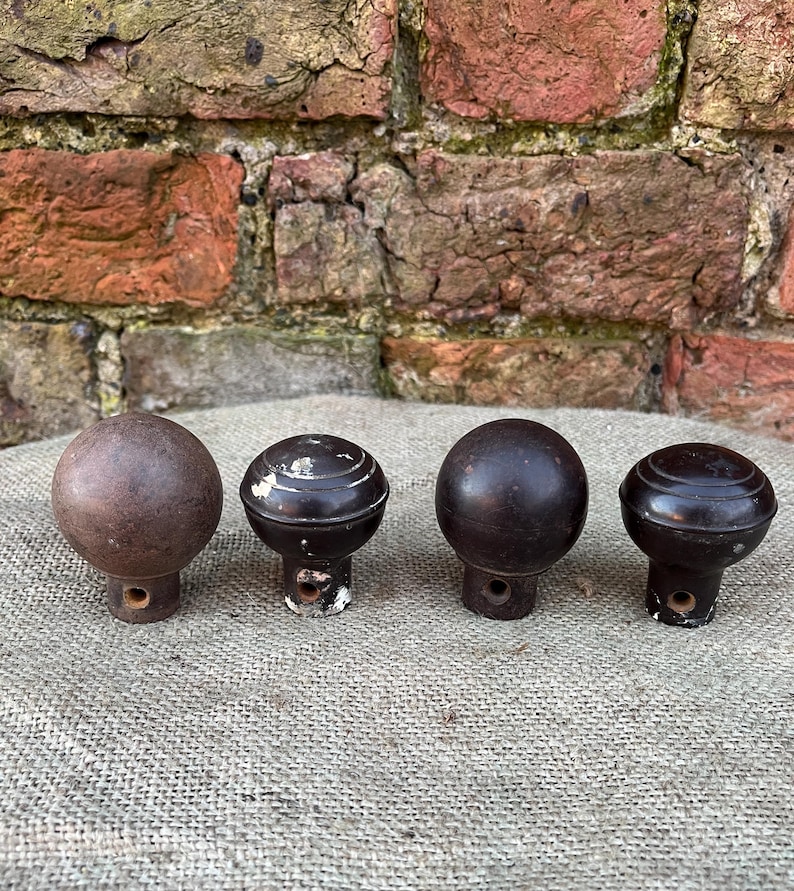 Może przedstawiać: Cztery antyczne, brązowe, drewniane gałki o okrągłym kształcie i małym otworze u podstawy. Gałki mają wygląd postarzałego, z widocznymi śladami zużycia i ubytkami farby. Ułożone w rzędzie na teksturowanej powierzchni.