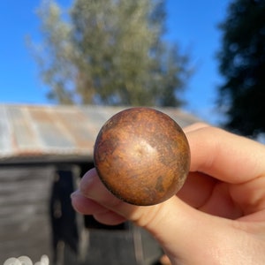 May include: A close-up of a round, wooden knob with a brown and gold finish. The knob has a smooth, polished surface.