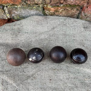 Może przedstawiać: Cztery antyczne drewniane gałki w r&oacute;żnych odcieniach brązu. Gałki ułożone są w rzędzie na teksturowanej, neutralnej powierzchni. Gałki mają okrągły kształt, niekt&oacute;re z płaskim, tarczowatym wzorem.