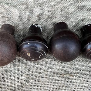 Może przedstawiać: Cztery antyczne drewniane n&oacute;żki meblowe w r&oacute;żnych odcieniach brązu. N&oacute;żki mają zaokrąglony, pękaty kształt z cylindrycznym wierzchem. Niekt&oacute;re wykazują ślady zużycia, z widocznymi niedoskonałościami i jasnymi plamami.