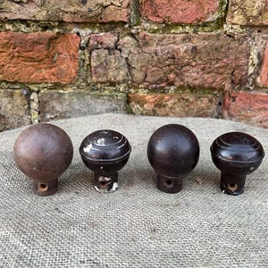 May include: Four antique wooden knobs in shades of brown. The knobs have a round shape with a decorative base and a hole for mounting. They are arranged on a neutral-coloured fabric.