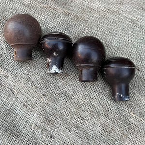 Może przedstawiać: Cztery zabytkowe brązowe drewniane gałki z zaokrąglonym wierzchem i cylindryczną podstawą. Gałki ułożone są w rzędzie na teksturowanej, neutralnej powierzchni. Niekt&oacute;re gałki noszą ślady zużycia z odpryskami farby.