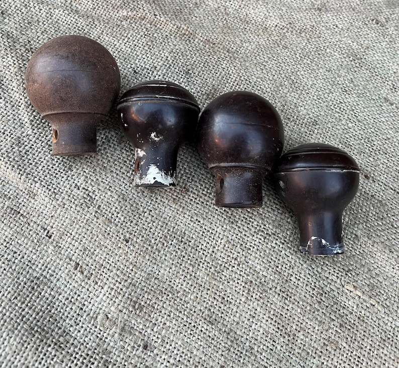 Może przedstawiać: Cztery zabytkowe brązowe drewniane gałki z zaokrąglonym wierzchem i cylindryczną podstawą. Gałki ułożone są w rzędzie na teksturowanej, neutralnej powierzchni. Niekt&oacute;re gałki noszą ślady zużycia z odpryskami farby.