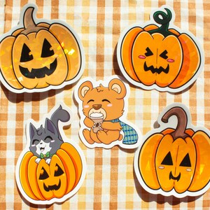 May include: Four Halloween-themed stickers featuring a cat, a bear, and two pumpkins. The cat is wearing a green bow tie and is inside a pumpkin. The bear is holding a cup of coffee. The pumpkins have orange and yellow colors and have spooky faces.