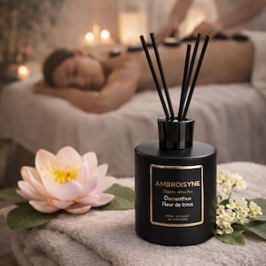 Peut inclure: Un diffuseur noir avec le texte "AMBROISYNE" et "Osmanthus Fleur de lotus" est posé sur une serviette grise pliée. Une fleur de lotus rose et de petites fleurs blanches sont à côté du flacon. Des bâtonnets noirs sont insérés dans le flacon.