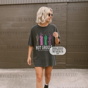 Op de afbeelding: Donkergrijs t-shirt met een afbeelding van vier middelvingers in verschillende kleuren. De tekst "HOT GHOULS" en "HEX THE PATRIARCHY" staan eronder. Ontwerp van BLACKFORDTATTOO, verkrijgbaar op Etsy.