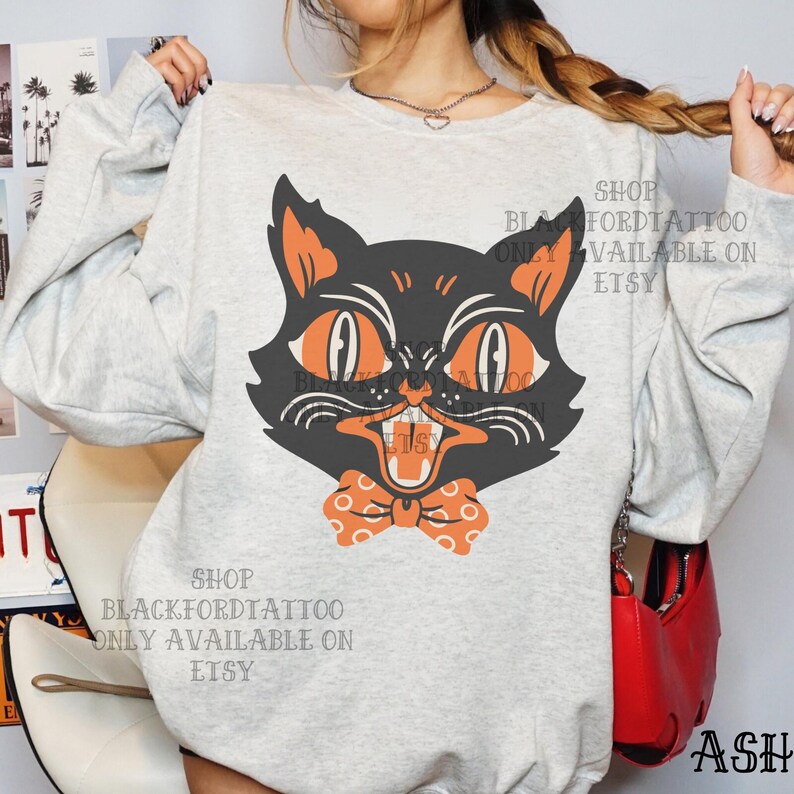 May include: A light gray sweatshirt featuring a black cat graphic with orange eyes and a bow tie. The cat has an open mouth and a slightly angry expression. The text "SHOP BLACKFORDTATTOO ONLY AVAILABLE ON ETSY" is printed on the sweatshirt.