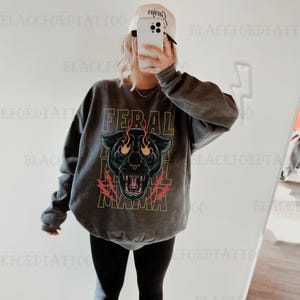 May include: A gray sweatshirt with a black panther graphic and the text "FERAL NAMA" in yellow. The panther has red flames coming from its eyes.