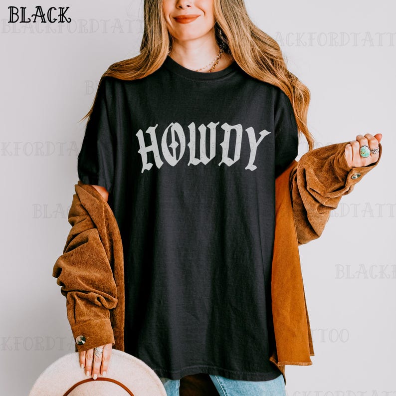 May include: A black t-shirt with the word "Howdy" printed in white on the front. The shirt is being worn by a person with long brown hair.