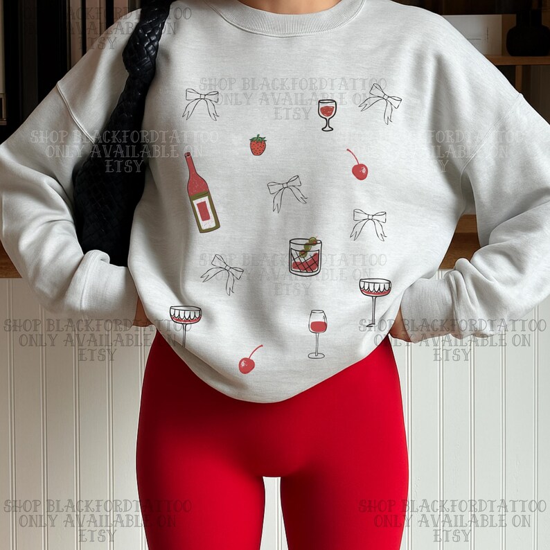 May include: A light gray sweatshirt with a pattern of wine glasses, bows, cherries, and a bottle of wine. The text "SHOP BLACKFORDTATTOO ONLY AVAILABLE ON ETSY" is printed around the design. The person is wearing red leggings.