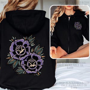 Peut inclure: Sweat à capuche noir zippé avec un motif de tatouage de rose violette sur le dos et à l'avant. Les roses sont dans un style de tatouage vintage avec des feuilles et des accents verts. Le sweat à capuche a une capuche à cordon.