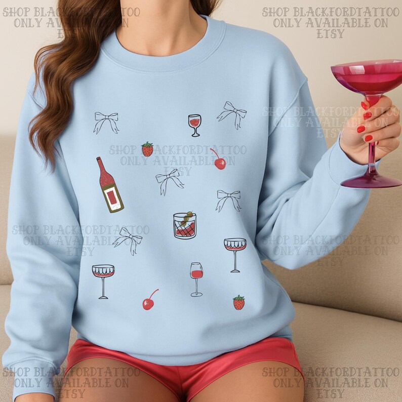 May include: Light blue sweatshirt with a pattern of cocktail-related illustrations, including wine glasses, cherries, strawberries, bows, and a bottle. The text "SHOP BLACKFORDTATTOO ONLY AVAILABLE ON ETSY" is printed around the design.